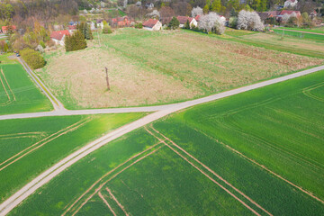 Droga polna przebiegająca przez pola i łąki widziana z wysokości. Zdjęcie z drona. W oddali widać zabudowania pobliskiej wioski. - obrazy, fototapety, plakaty