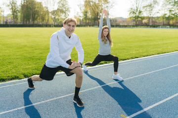 Fototapeta premium Young sports couple trains at the stadium in summer. Doing various stretching exercises. Fitness. The concept of a healthy lifestyle