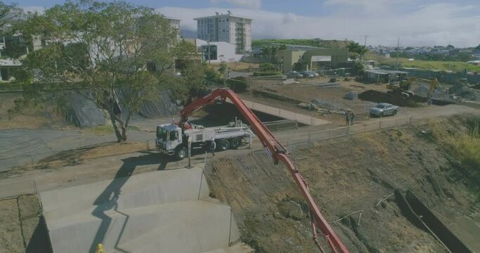 large boom concrete pump pouring concrete on large slab and construction workers, drone shot, cement slab construction, cement mixer truck, cement ramp construction on lot