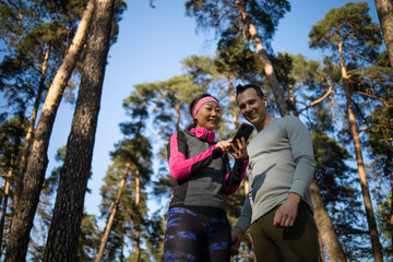 Two runners checking achievements on mobile phone app in forest 