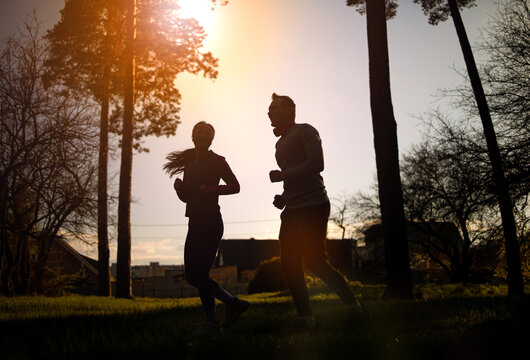 fitness, sport, people and lifestyle concept - couple running outdoors at sunset, silhouette image.