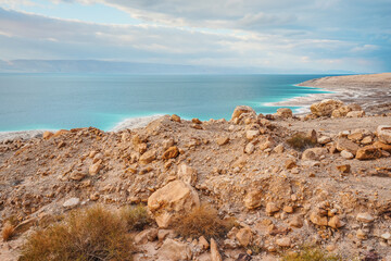 Dead sea shore at Jordan side, dry sand and rocks beach, sun shines on beautiful azure water surface