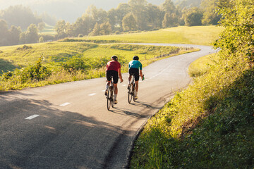 Fototapeta premium Two road cyclists, male and female during training at beautiful nature landscape at sunset, back view