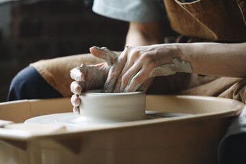 Potter's hands molding clay vase on pottery wheel, ceramic studio workshop, traditional pottery making