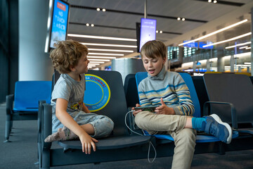 Children play games and watching cartoons on tablet or smartphone, while waiting for their airplane flight in airport. Family travel by air with child.