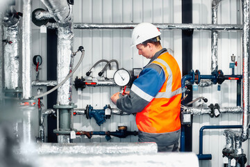 Operator of gas boiler house in helmet and protective vest checks pressure readings of pressure...
