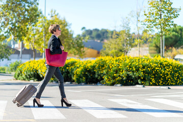 Traveling elegant businesswoman wearing sunglasses crossing street