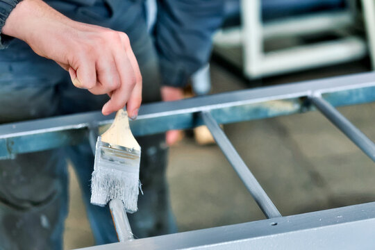 Working painter paints metal ladder with paint brush. Hand close-up with space for copying. Industrial background.