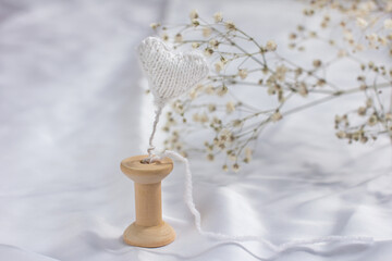 Fototapeta na wymiar A gypsophila branch and a knitted white heart. Wooden Spool for Thread