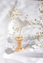 A gypsophila branch and a knitted white heart. Wooden Spool for Thread