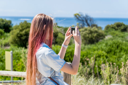 Generation Z Teenage girl with pink ombre colored hair making photo video of beautiful landscape on a phone for social media