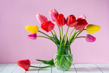 Bouquet of beautiful tulip flowers in a transparent glass vase on a pink background