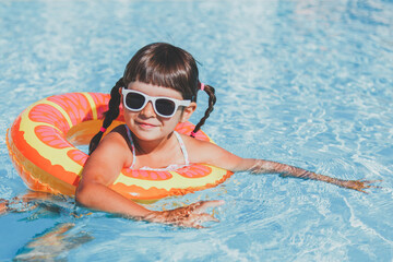 close-up portrait of a toddler girl 4 years old swims in the pool in the summer in an inflatable circle and looks at the camera, vacation concept