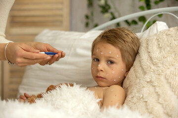 Toddler boy with chicken pox,lying in bed with fever, mother checking him