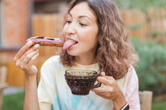 Happy woman eating delicious tasty eclair cake and drinking tea in outdoor cafe