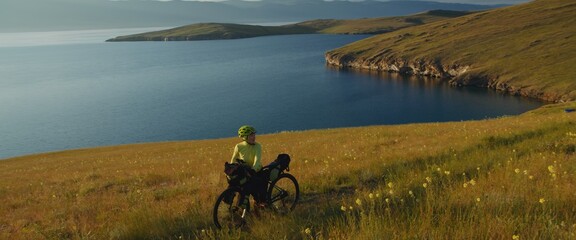 The girl towing gravel bike at picturesque sunset. The woman travels on a bicycle with bikepacking...