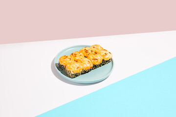 Hot maki roll with cheese and sesame on coloured background. Baked sushi roll with salmon inside, sesame outside, cheese topped. Maki sushi in minimal style. Japanese menu concept.
