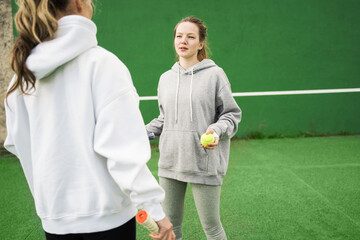 Female teenager holding racket and playing at tennis with her sporty mother