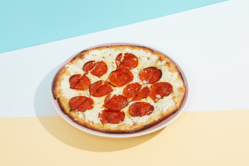Italian pizza with pepperoni and cheese on coloured background. Cheese focaccia with salami in minimal style on blue and orange color. American pizza delivery concept with color backdrop