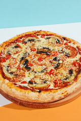 Italian pizza with mushroom and cheese on coloured background. Vegan pizza with mushroom and tomato in minimal style on blue and orange color. American pizza delivery concept with color backdrop