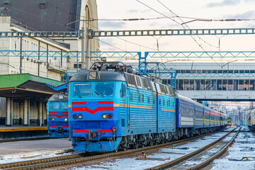 Two electric locomotives with passenger intercity trains stand at the platform of the railway...