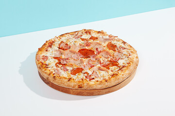 Italian pizza with ham and bacon on coloured background. Meat pizza with bacon and ham in minimal style on blue and orange color. American pizza delivery concept with color backdrop