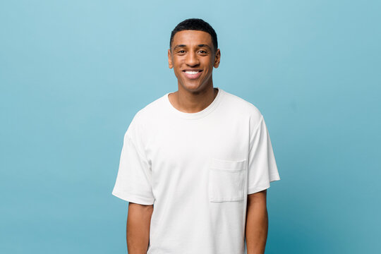 Portrait of cheerful young african-american guy wearing white casual t-shirt posing isolated on blue background. Carefree young millennial man looking at camera and laughing