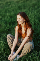 A young woman in summer clothes sitting on the green grass doing yoga and meditating in nature, a connection with the cosmos. The concept of harmony with body and nature, spiritual growth