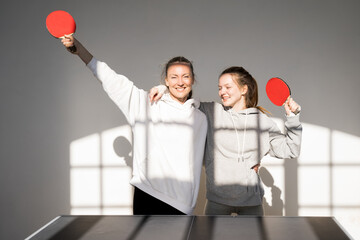 Mother and daughter embracing and looking at camera while playing ping pong