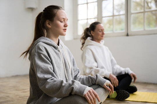 Woman meditating at the yoga mats with her teen daughter while having yoga training