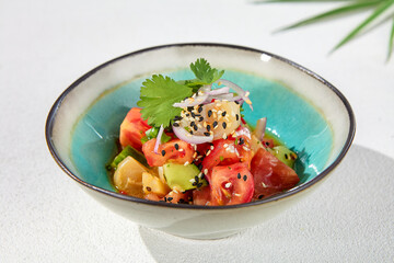 Vegetables salad with tomatoes, cucumbers and onion on white table with hard shadow. Vegan starter in asian style. Summer menu concept. Asian food in minimal design with sun light shadow.