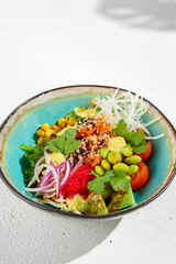 Hawaiian cuisine - Poke bowl with salmon, avocado, edamame and vegetables. Pokebowl in ceramic dish on white background with leaves. Summer menu in asian style. Healthy food.
