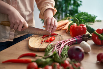 Woman cutting chili peppers on wooden board