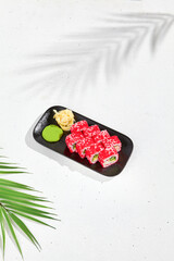 Modern asian food - alaska maki sushi on black plate on white concrete background. Sushi roll with crab, avocado, cucumber inside and tobiko caviar outside. Maki sushi with masago caviar.