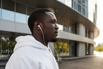 Profile portrait of young African American man in white hoodie and earphones looking into the distance outdoors