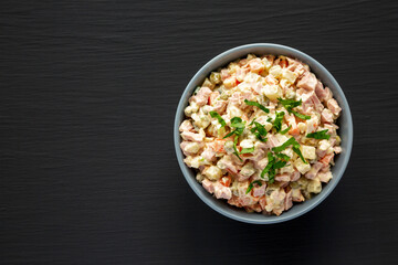 Homemade Olivier salad in a Bowl on a black wooden surface, top view. Flat lay, overhead, from above. Space for text.