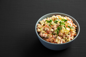 Homemade Olivier salad in a Bowl on a black wooden surface, side view. Space for text.