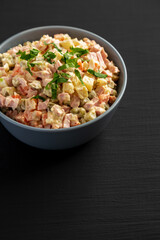 Homemade Olivier salad in a Bowl on a black wooden background, side view. Copy space.