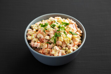 Homemade Olivier salad in a Bowl on a black wooden surface, side view.