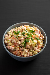 Homemade Olivier salad in a Bowl on a black wooden background, side view.