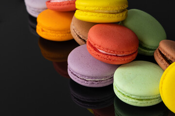 Lots of colorful macaroons on black background with reflection. Traditional french dessert