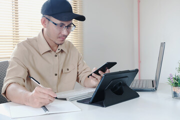 Man using a laptop computer and phone at work in a office, online study, internet marketing, working from home, office workspace freelance concept