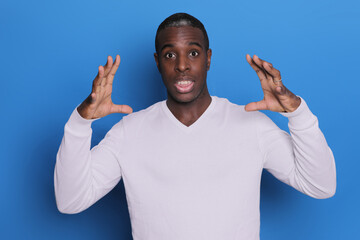 Fototapeta premium Indoor photo of young African American man pictured isolated on blue background with hands near head