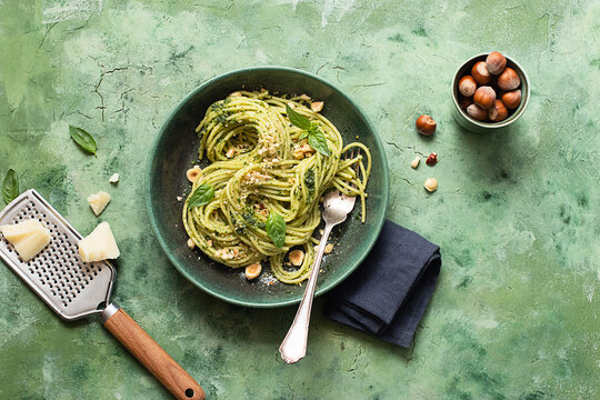 Ceramic plate with hazelnut pesto spaghetti on green table surface