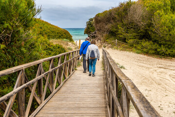 Majorca. Platja de Muro beach on a cloudy day. Wooden platform on the beach. A couple of elderly people go to the sea