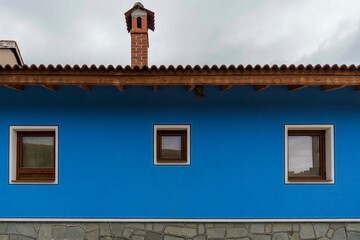Wall of a house painted blue,three windows,chimney