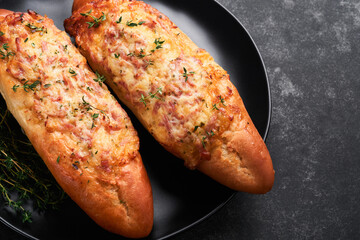 Baguette boats. Hot baked sandwich on baguette bread with ham, bacon, vegetables and cheese on parchment and black dark concrete background. Top view. Copy space.