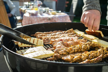 Hot grill cheese is turned over with tongs, next to it lies meat on sticks on the grate. Cooking food on the barbecue, outdoor. 