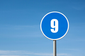 '9 (nine)' sign in blue round frame. Clear sky is on background