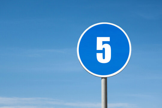'5 (five)' sign in blue round frame. Blue sky is on background